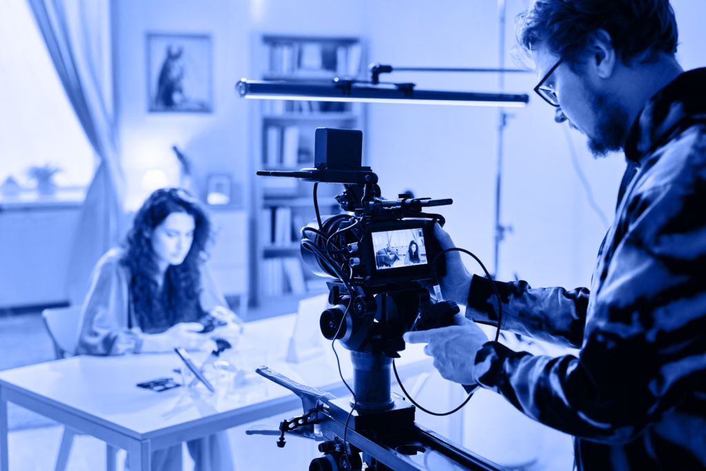 Image of a videoshoot in progress with a cameraman recording a woman at a desk